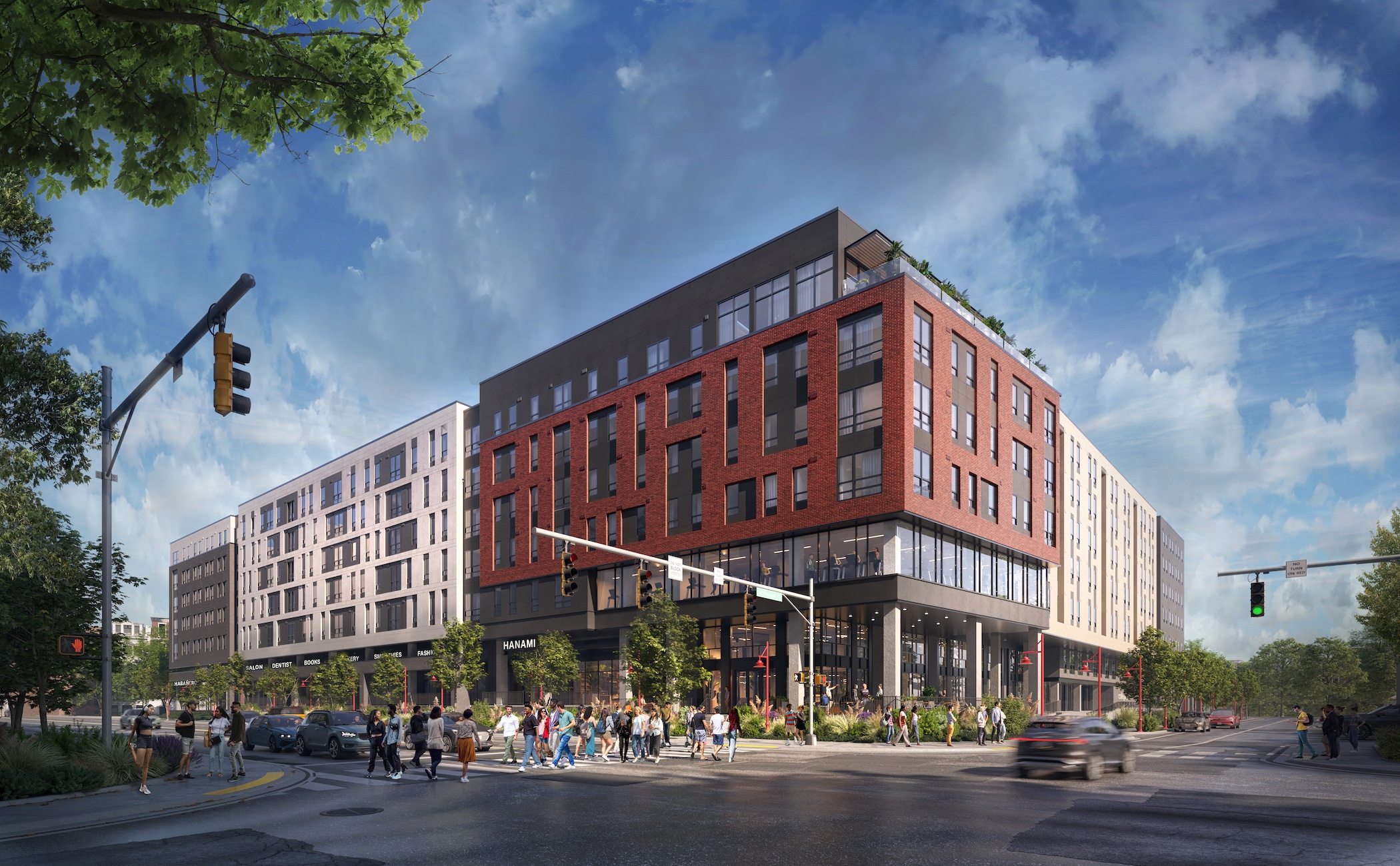 A modern multi-story apartment building, Rambler College Park North, with red and gray exterior stands at a busy city intersection, as people walk on sidewalks and cars wait at traffic lights under a blue, partly cloudy sky.