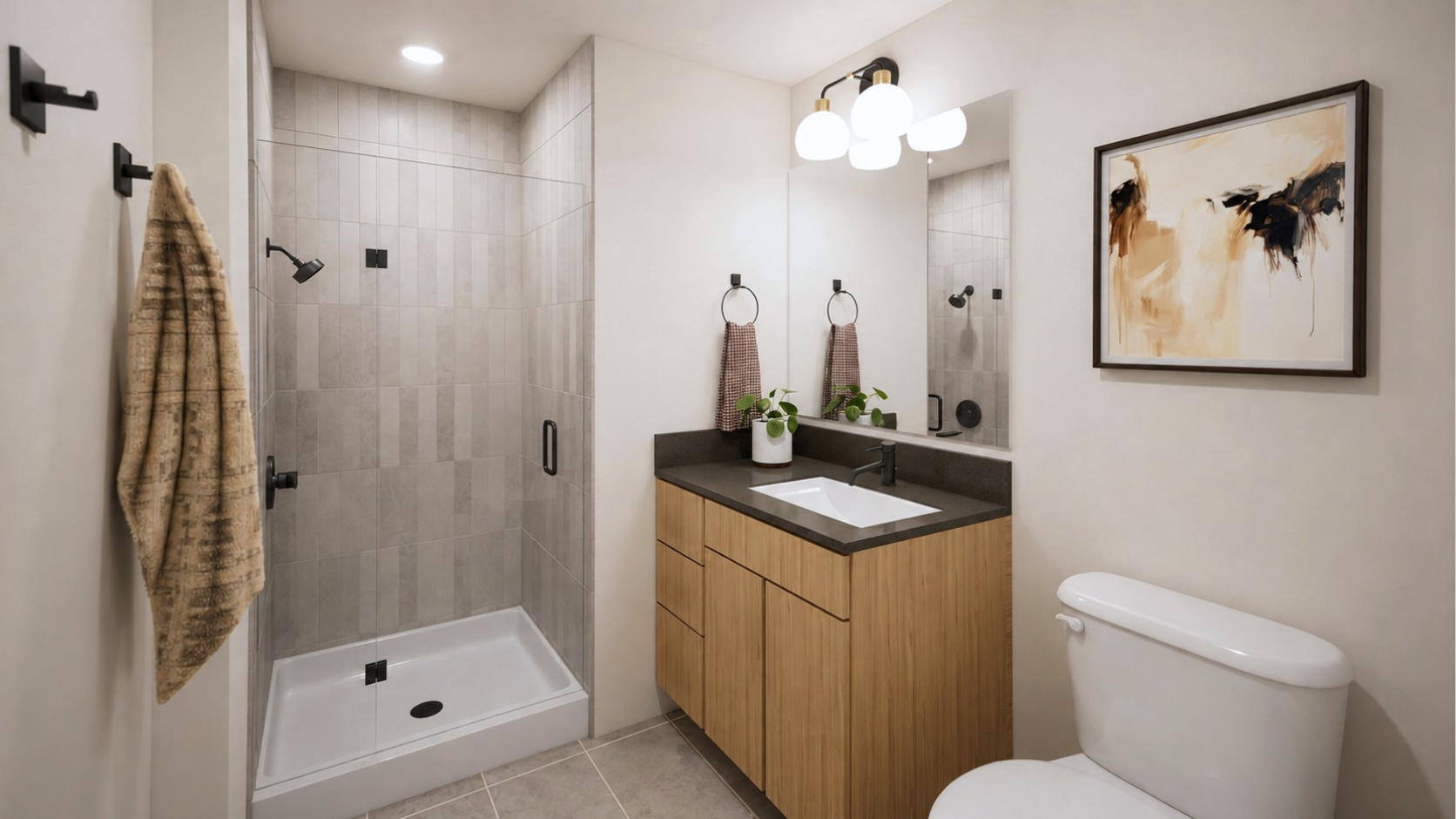Modern bathroom at Rambler College Park North with a glass shower, wood vanity with a plant, round mirror, white toilet, abstract art on the wall, towels, and bright overhead lighting.