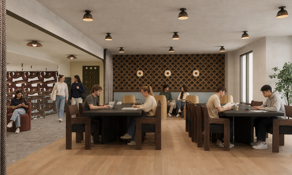 People study and read at dark wood tables in a modern, well-lit study area with geometric wall decor in Rambler College Park South. Some individuals walk or sit in an adjacent lounge area, while large windows let in ample natural light.
