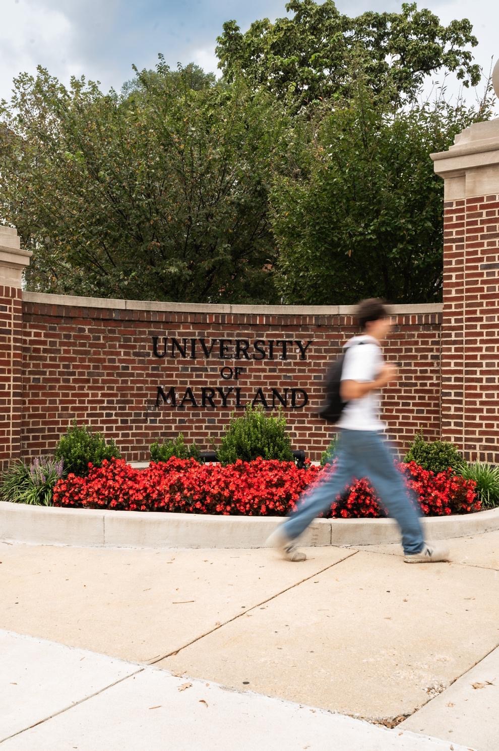 Five young women in red and black University of Maryland apparel hold hands and smile while walking in front of the Maryland Terrapins stadium entrance, excited to return to their best student apartments near UMD.